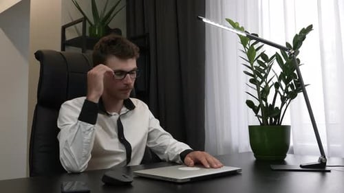 Tired overworked man is finishing to work in office and closing laptop computer.