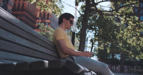 Man sits on park bench while using phone