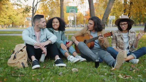 Young Men and Women Playing the Guitar Singing Enjoying Autumn Day in Park