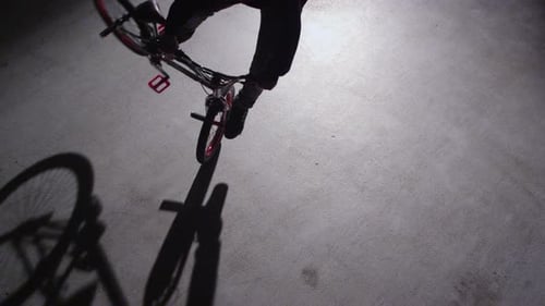BMX rider doing tricks in dark warehouse.