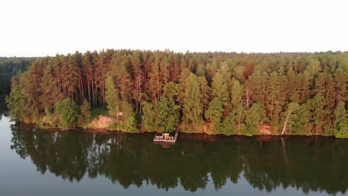 Kiefernwald in den Strahlen der untergehenden Sonne mit Häusern, umgeben von Bäumen am Ufer des Sees