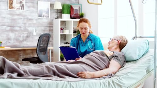 Social Worker Consulting an Elderly Disabled Woman Who Lies in Hospital Bed