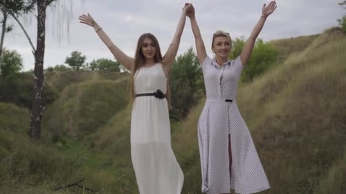 Women Hold Hands in Sunny Field with Rolling Hills