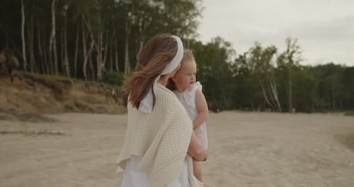 Mother and Baby Daughter Walk on the Beach Near the Sea Together Embracing