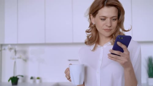 Woman Uses Phone and Drinks Coffee in Kitchen