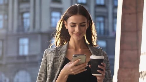 Smiling Woman Using Phone with Coffee Outdoors