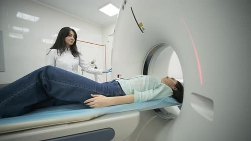 Female patient is undergoing CT or MRI scan under supervision of a radiologist