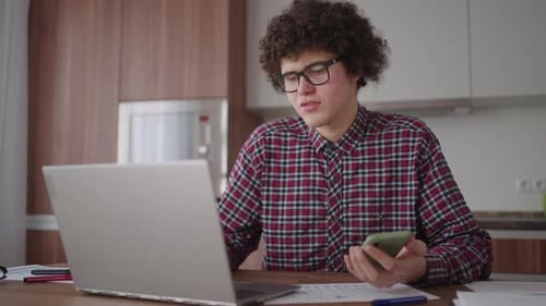 Young Adult Using Laptop and Smartphone in Kitchen