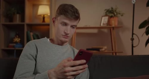 Crop View of Amazed Millennail Man Scrolling Phone Screen While Sitting on Sofa at Home