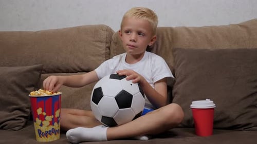 Blond Boy Watching Soccer and Eating Popcorn