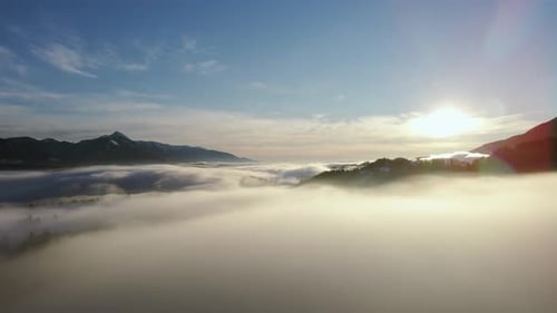 Drone shot of an incredible landscape covered under the fog with surrounding mountains in the morni