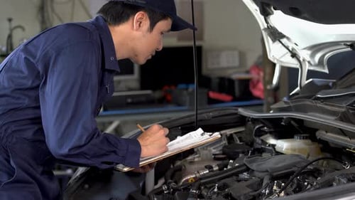male mechanic checking and repair service a car with clipboard
