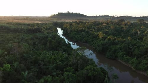 Un Drone survole une rivière, au milieu de la forêt amazonienne, tandis que des nuages apparaissent à l'horizon