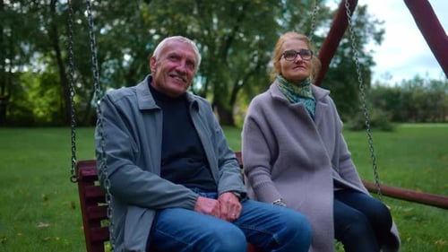 Old Couple Sitting On A Swing In The Park. - close up