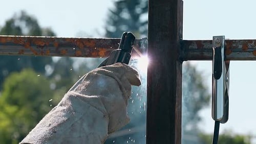 Closeup Worker in Gloves Welds Metal Carcass of Fence
