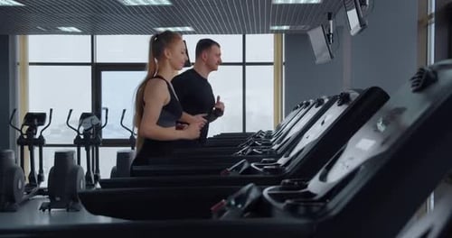 A Man And A Girl Go In For Sports In The Gym. Running On A Treadmill