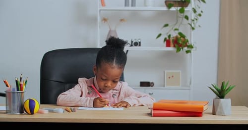 Kleines lustiges Vorschulmädchen Kreatives talentiertes afroamerikanisches Kind, das alleine am Tisch sitzt