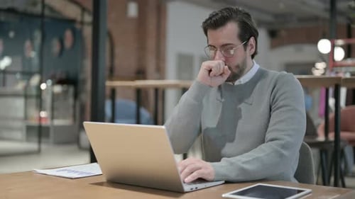 Young Man Coughing While Using Laptop in Office