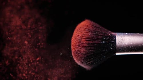 Make-up-Pinsel mit farbigem rotem Pulver auf schwarzem Hintergrund Zeitlupe
