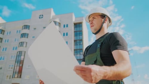 A Man in a Helmet Is Holding a Construction Plan in His Hands
