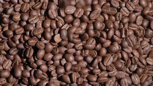 Freshly roasted coffee beans or coffee grains fall on a wooden table on a brown background at cafe.