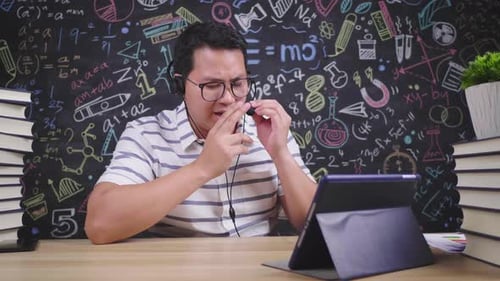 Front view of Asian man having a meeting online on tablet and using wireless microphone at home