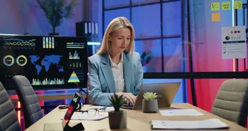 Businesswoman Working on Laptop and Making Important Notes Inot Paper Report in Evening Office