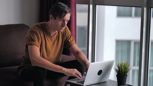Man Types on Laptop at Home During the Day