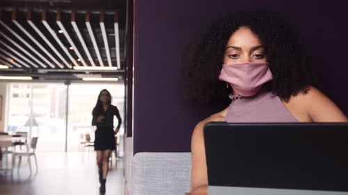 Femme d'affaires portant un masque travaillant dans une cabine socialement éloignée au bureau pendant la pandémie de santé