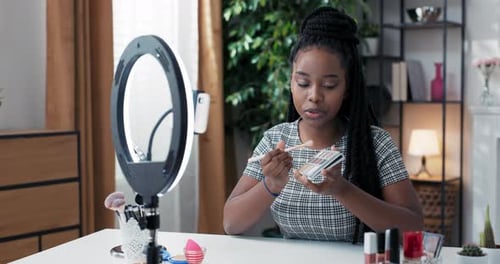 Mujer bloguera de belleza filmando tutorial de rutina de maquillaje de ojos diario cerca de la cámara del teléfono