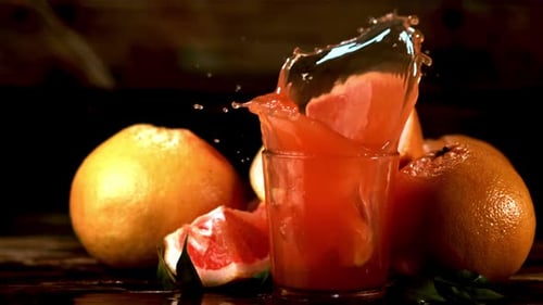 Cámara lenta en un vaso con jugo de toronja cae un trozo de toronja con spray