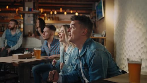 Friends are Watching Together Emotionally Watching Football on TV in a Bar and Celebrating the