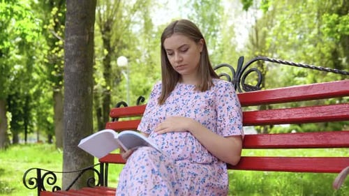 Pregnant Woman in a Summer Dress with a Floral Print Walks in the Park