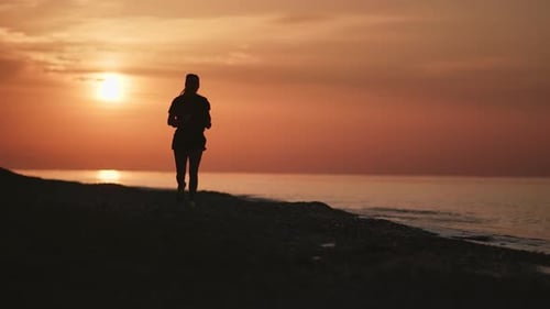 Fitness Woman Running on Morning Beach with Dramatic Sunrise Sky