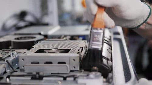 Nahaufnahme von männlichen Händen, die mit einer Bürste an der Demontage und Reinigung der Leiterplatte im Laptop arbeiten