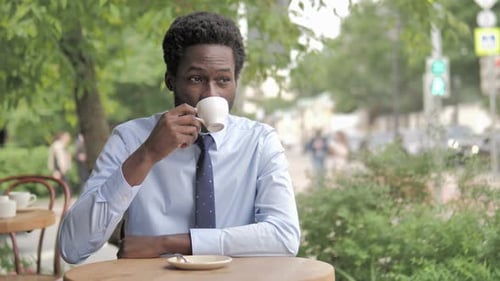 African Businessman Drinking Coffee while Sitting in Outdoor Cafe