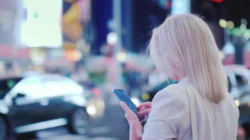 Vista traseira: Mulher de negócios usa um smartphone na movimentada Times Square, em Nova York. Os famosos táxis amarelos