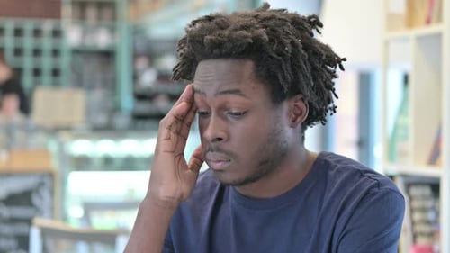 Young Man Rubs Temples in Cafe