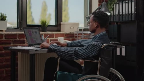 Man in Wheelchair Working at Desk With Laptop
