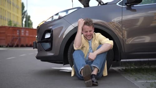 Angry guy sitting near the car with the hood open.
