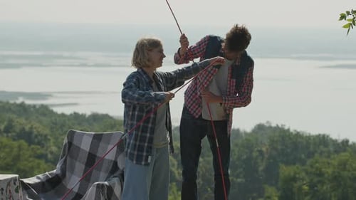 Young Adults Assembling Tent in Sunny Rural Landscape