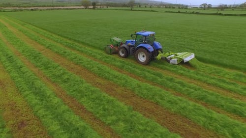 Luftaufnahme eines Traktors, der das Gras auf einer großen grünen Wiese mäht.