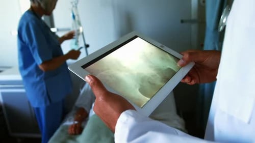 Männlicher Arzt gemischter Rasse, der in einem medizinischen Zentrum arbeitet, ein Tablet benutzt und einen Scan betrachtet, mit seinem