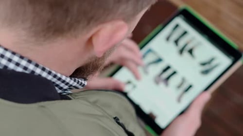 Man Is Examining Site of Online Shoe Store By Tablet View Through Shoulder