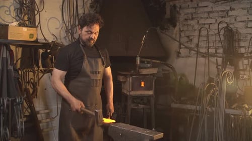 Portrait of Blacksmith in Working Atmosphere. Man Works with Molten Metal in the Forge
