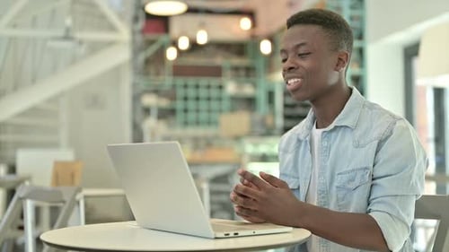 African Man Doing Video Chat on Laptop in Cafe