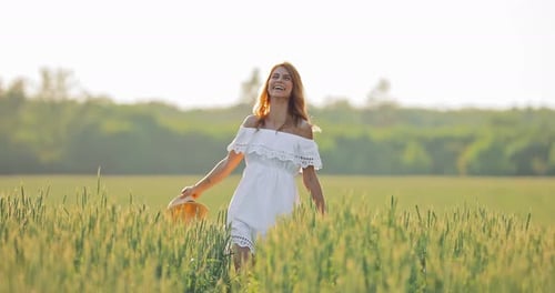 Beautiful Girl in a Hat and Dress Walks Across the Field in Summer