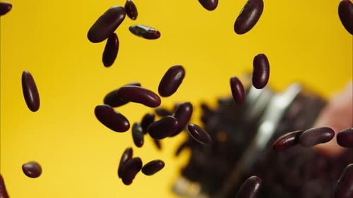 Closeup of Falling Down Red Beans on Glass Table From Jar on Yellow Background