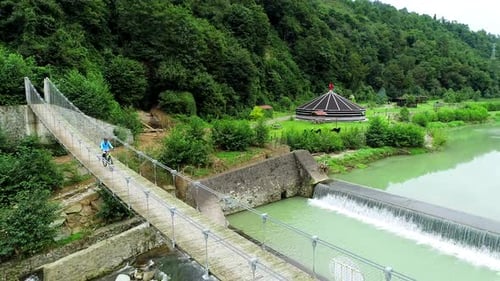 Biking Across Suspension Bridge in Green Rural Landscape