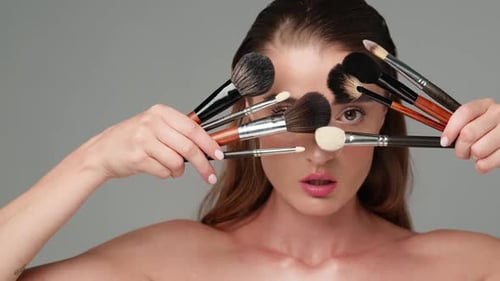 Attractive Woman with Makeup Brushes on Grey Background